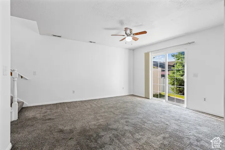 Carpeted living area featuring a ceiling fan with light, white wall finishes, and a sliding glass door