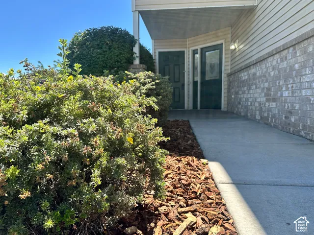 Siding exterior with a brick foundation, concrete walkway, and landscaped shrubs with bark mulch