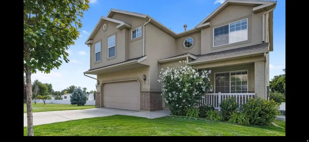Two-story stucco residence featuring a covered front porch with white railings, an attached two-car garage, and a concrete driveway