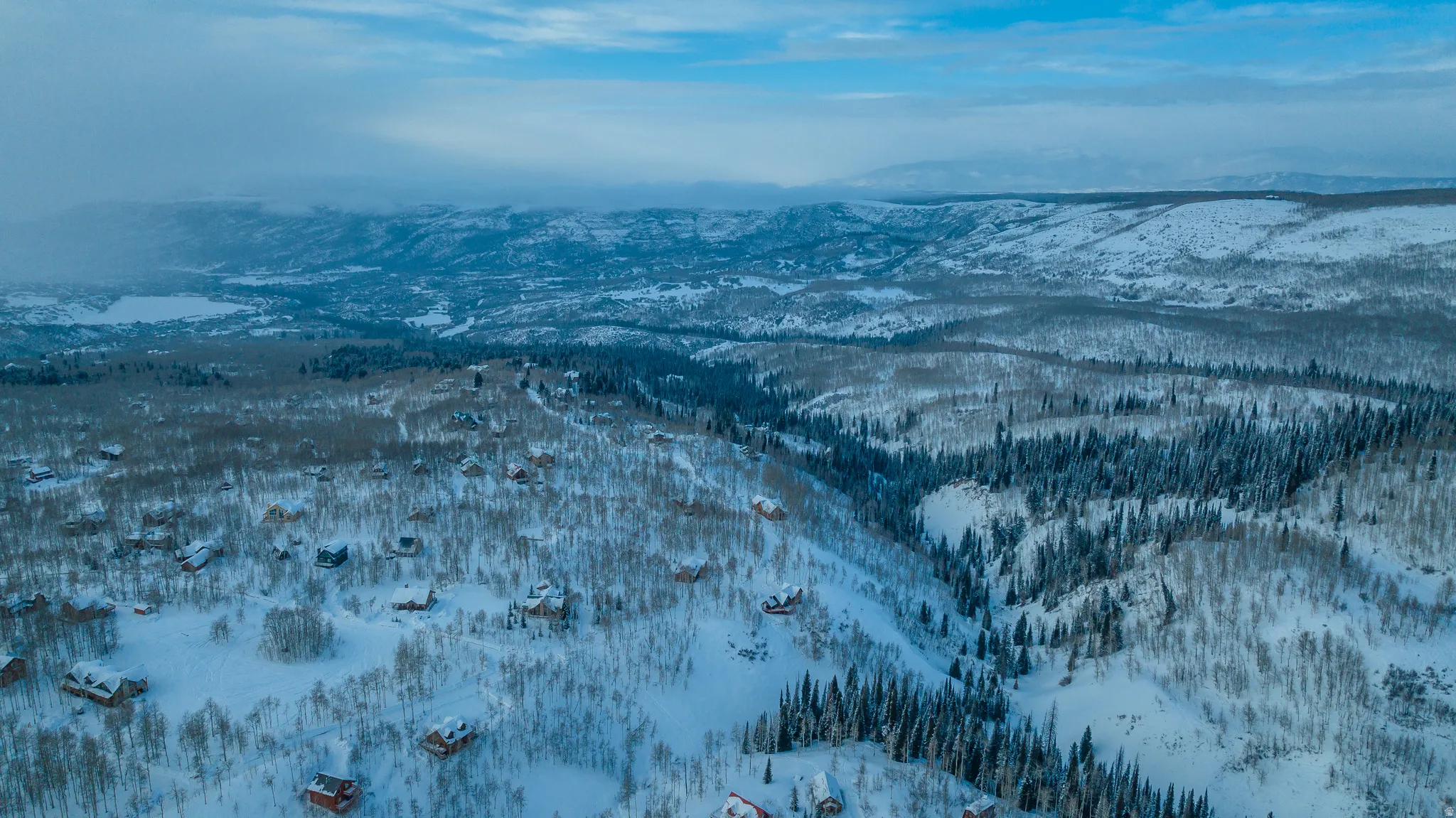 Snow-covered landscape featuring scattered residences amongst dense forests and mountainous terrain