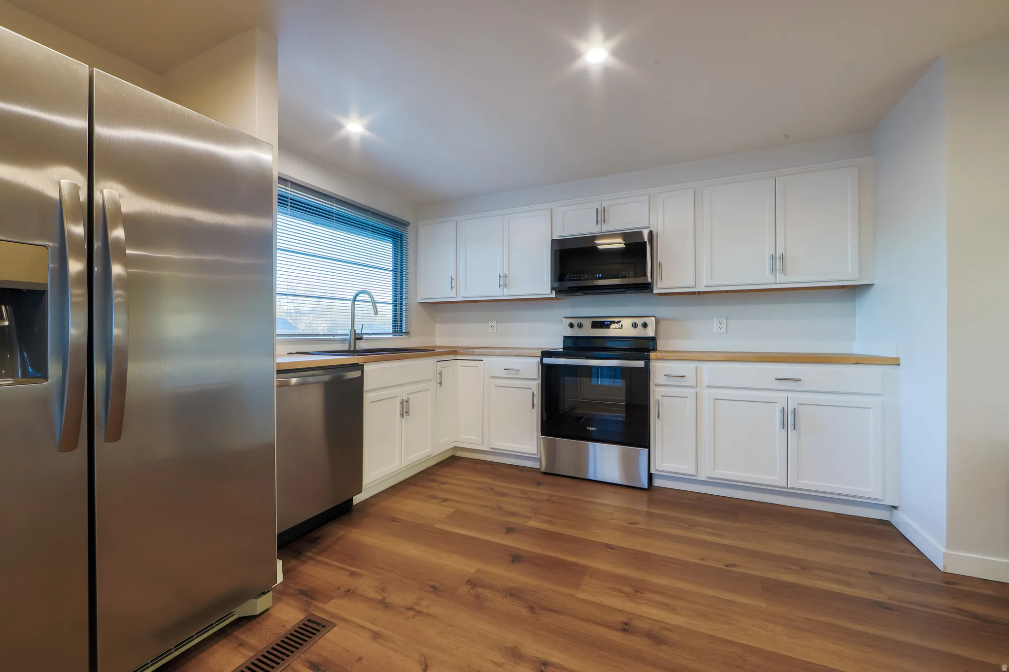 Kitchen featuring stainless steel appliances, white cabinets, light countertops, and dark wood-style floors