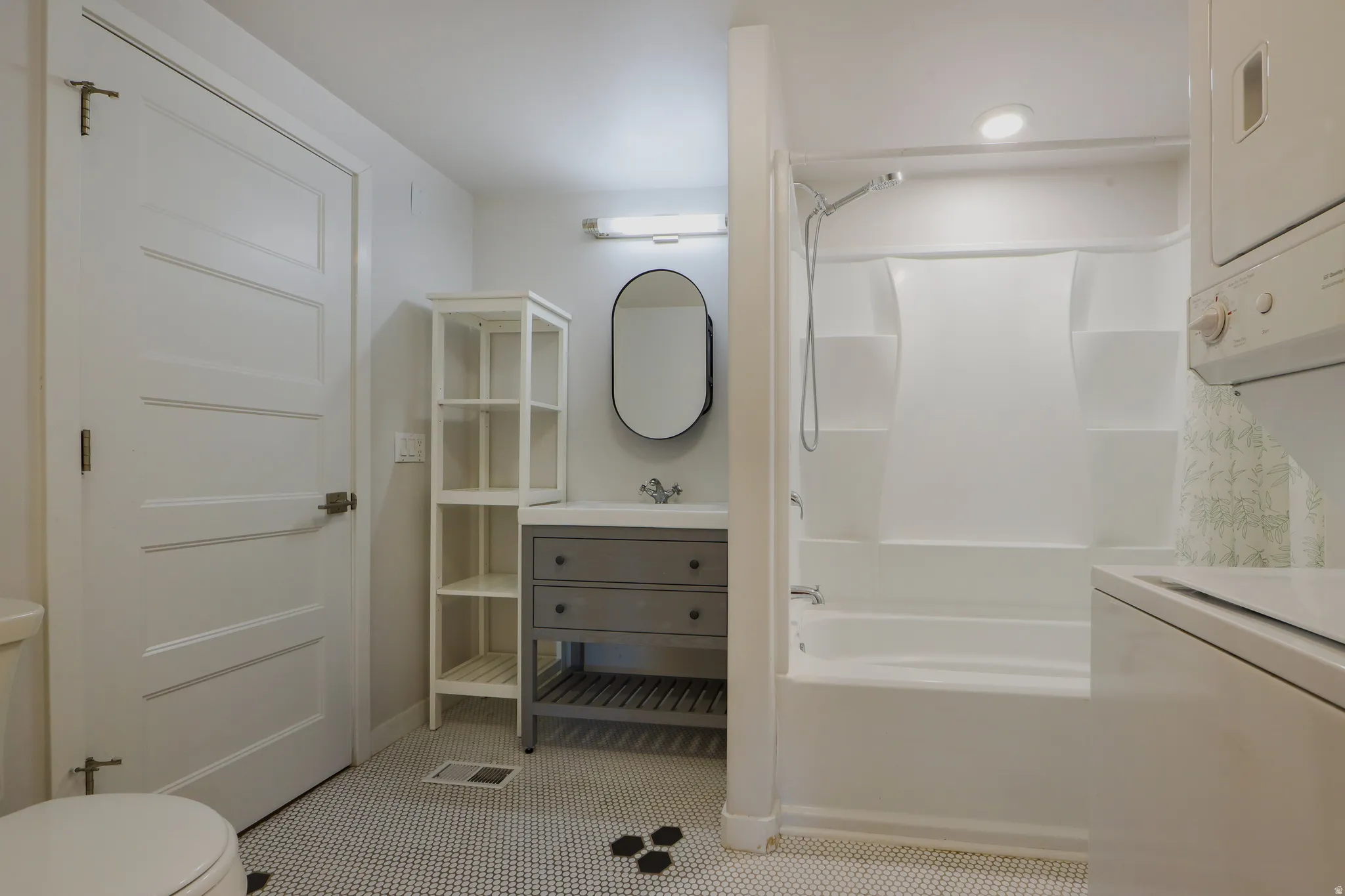 Full bathroom featuring vanity, stacked washing machine and dryer, shower / washtub combination, and light tile patterned flooring