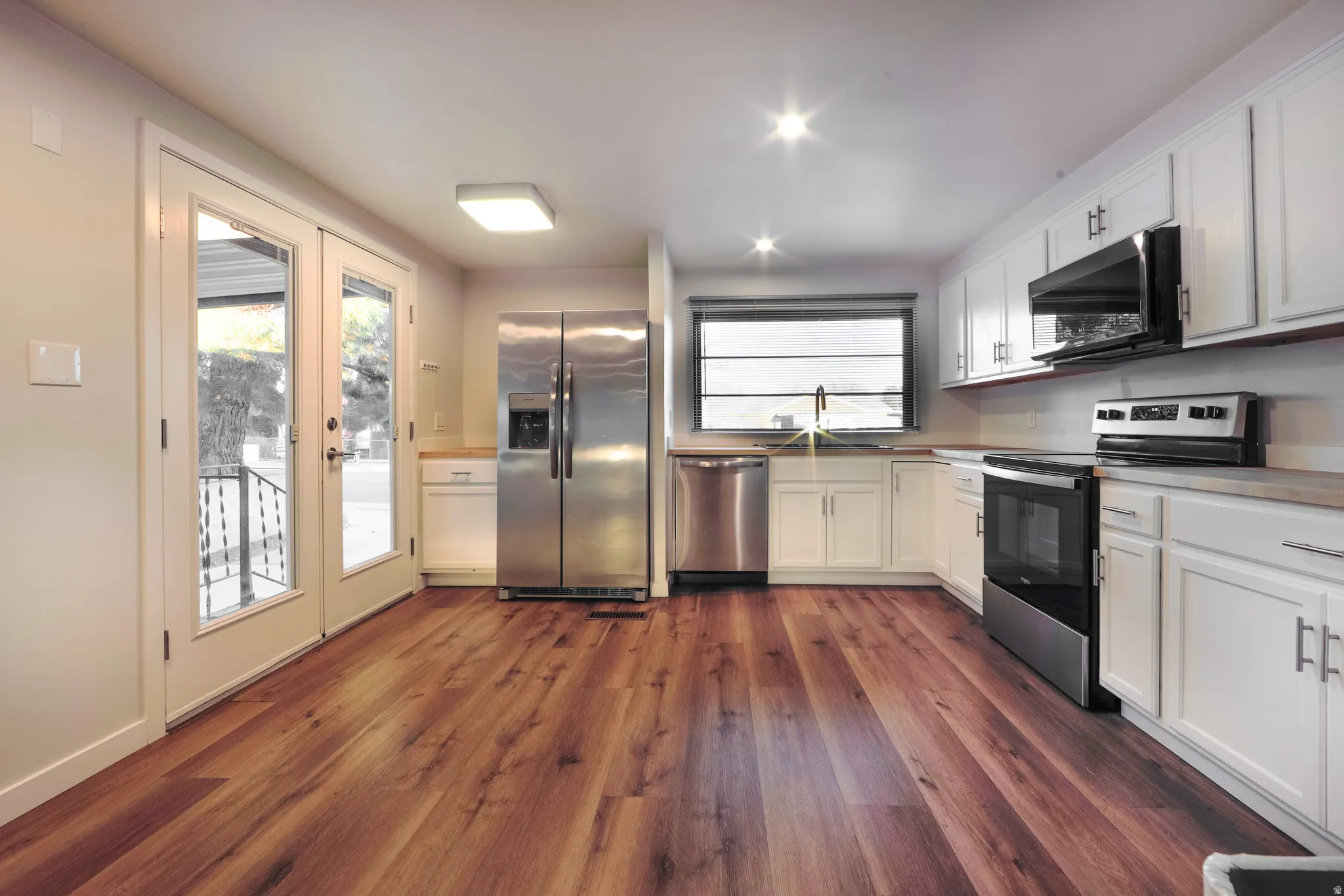 Kitchen with stainless steel appliances, white cabinets, light countertops, dark wood-type flooring, and recessed lighting