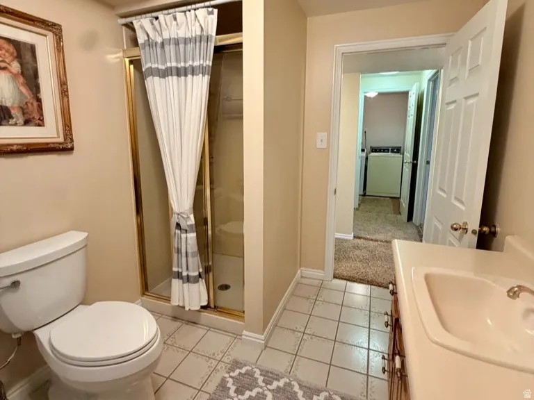 Bathroom featuring tile flooring, a glass-enclosed shower with gold-tone framing, a single-sink vanity with a built-in countertop, and a white toilet