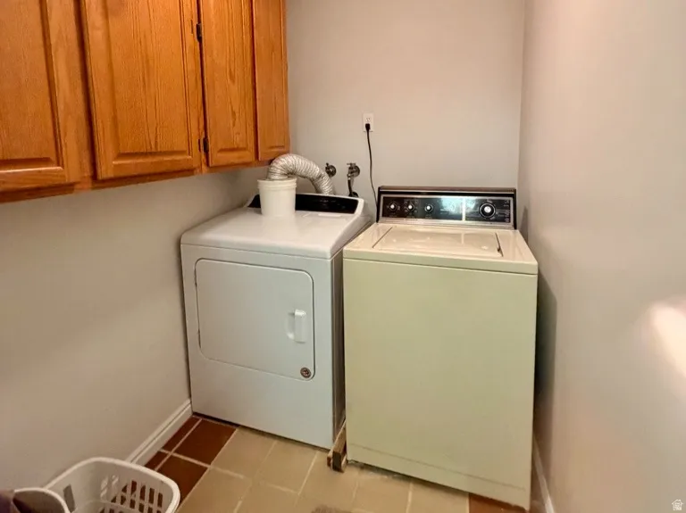 Dedicated laundry area featuring upper wood cabinetry, tile flooring, and a ceiling-mounted light fixture