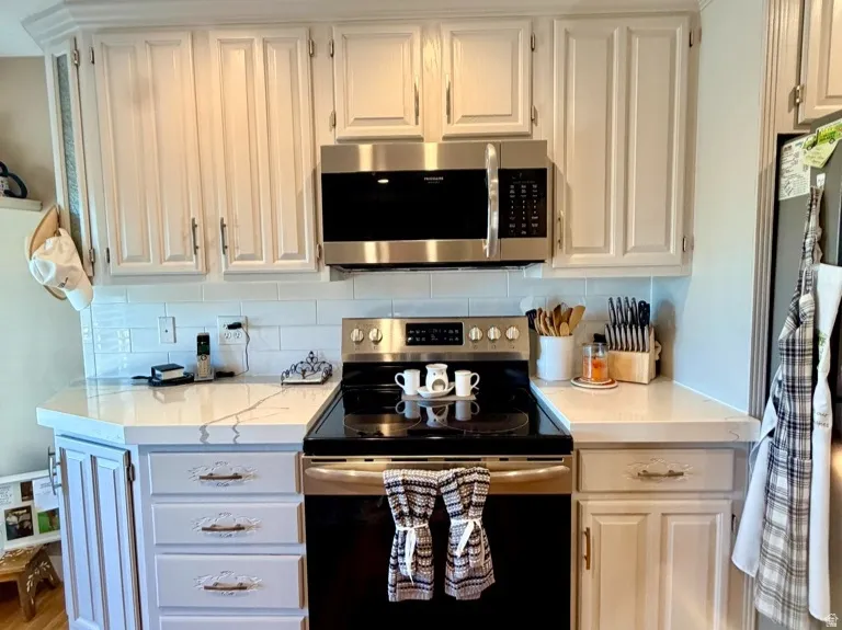 Kitchen featuring white cabinetry, stainless steel appliances, white countertop surfaces, a subway tile backsplash, and wood-finish flooring
