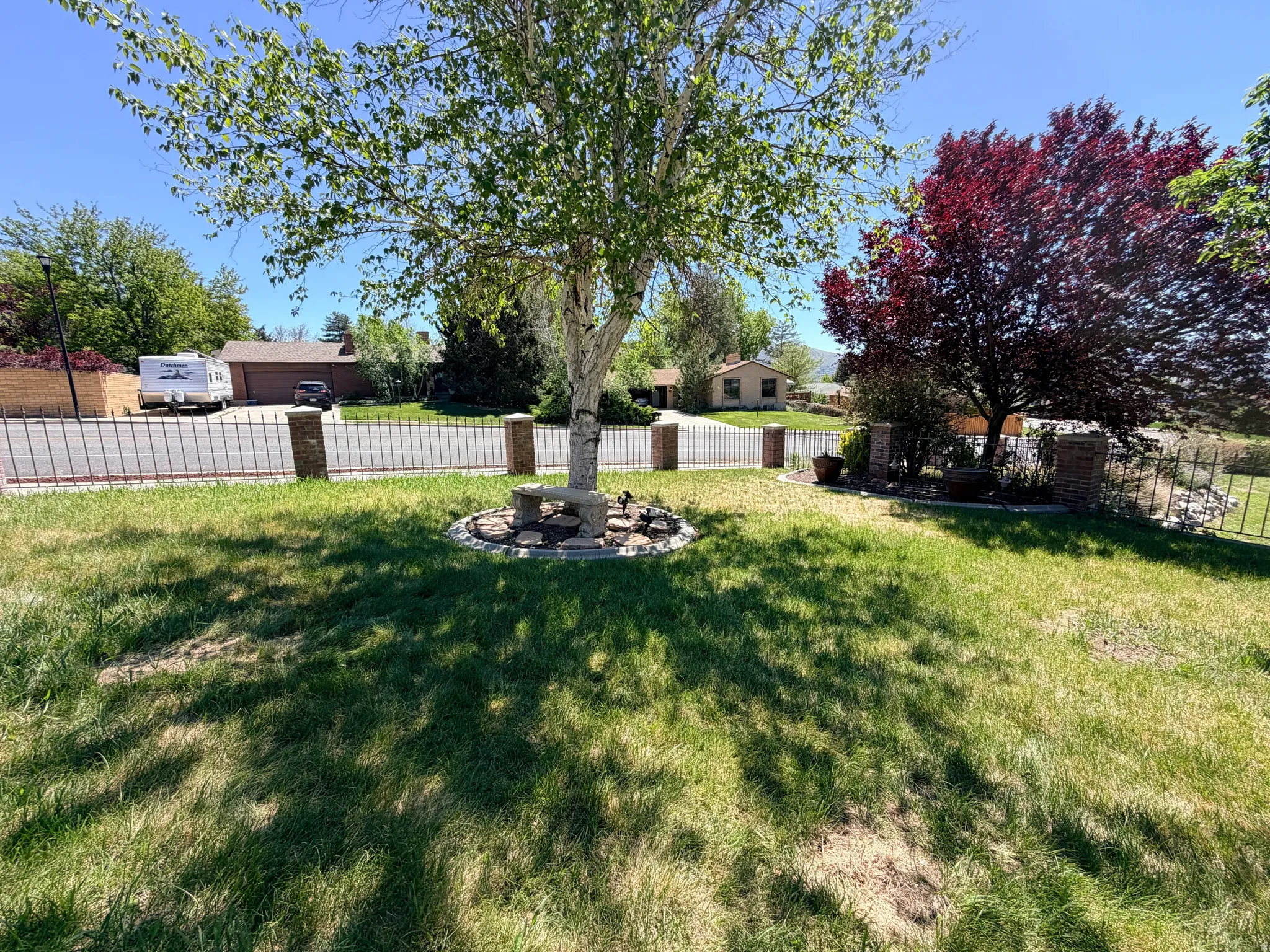 Front yard with mature trees, a decorative black metal fence, and brick pillar accents