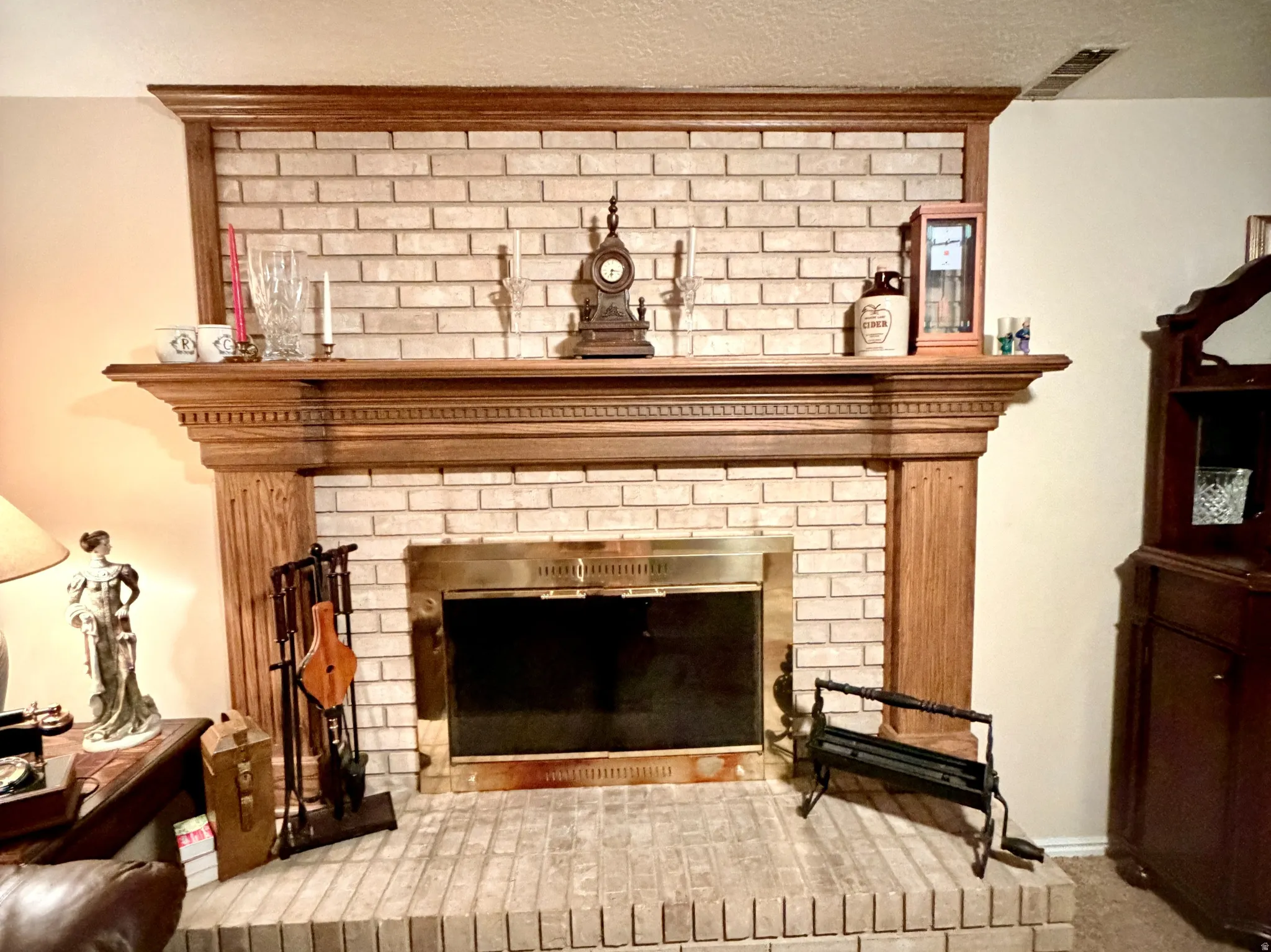 Fireplace featuring a light brick surround and hearth, a brass-framed firebox, and a detailed wood mantel
