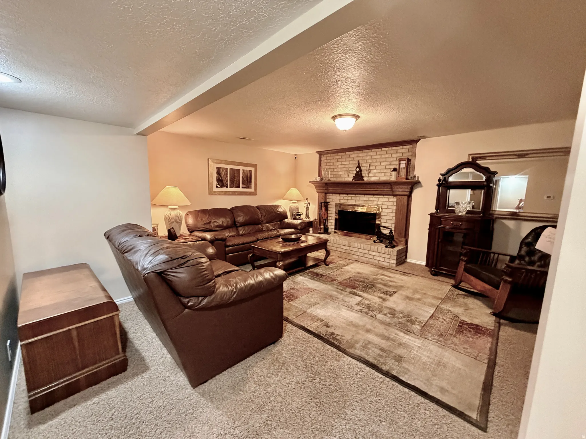 Carpeted living area featuring a brick fireplace with a wood mantel