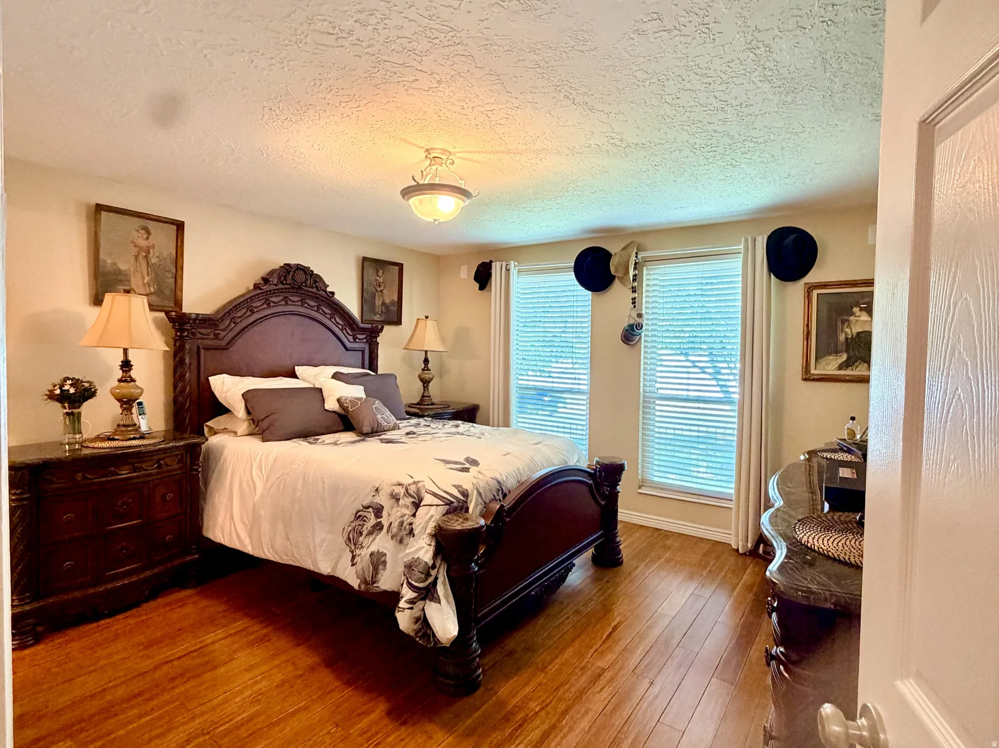 Spacious bedroom featuring wood-finish flooring, textured ceiling, and two windows with blinds providing natural illumination