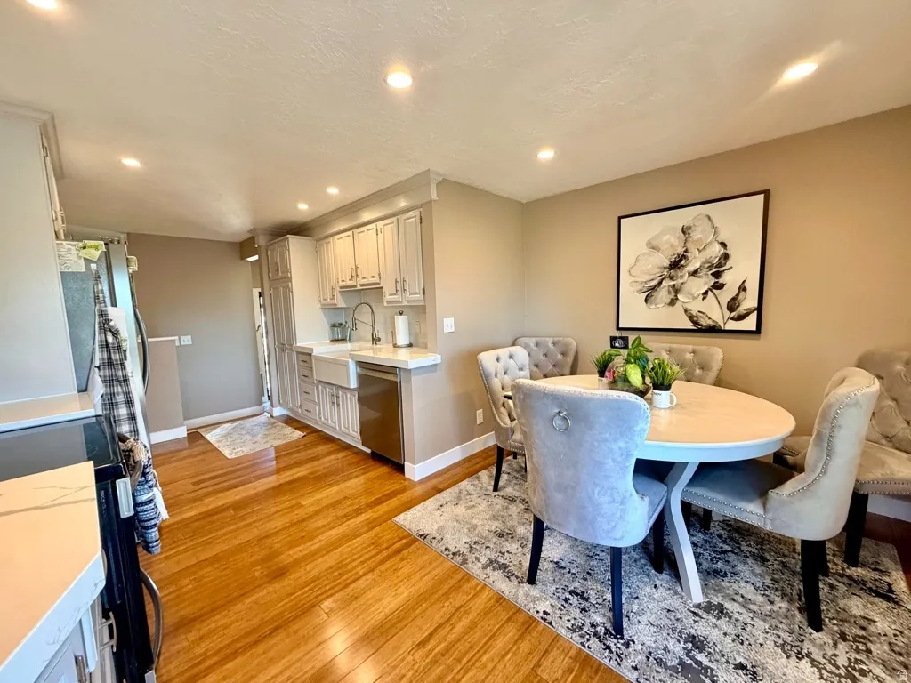 Open-concept kitchen and dining area featuring wood-finish flooring, recessed lighting, white perimeter cabinetry, a farmhouse-style sink, and stainless steel appliances
