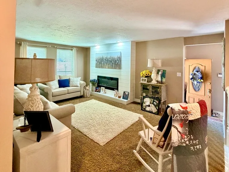Spacious living area featuring brown carpeting and a white shiplap fireplace surround