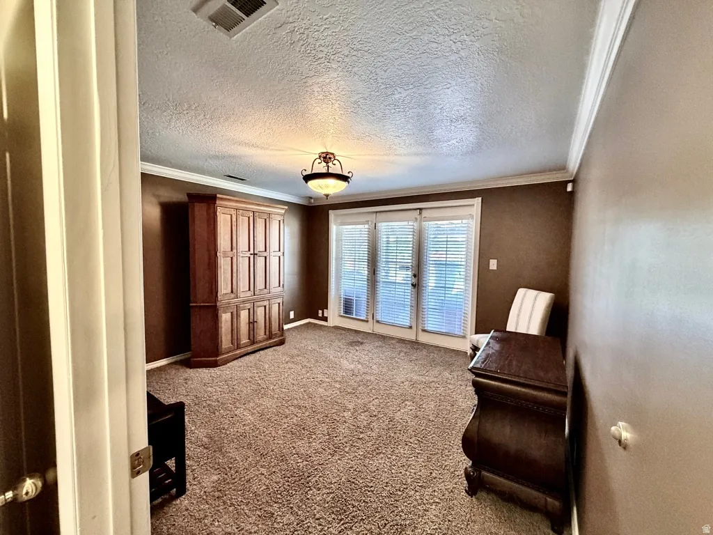 Spacious interior room featuring French doors with integrated blinds, crown molding, and textured ceilings