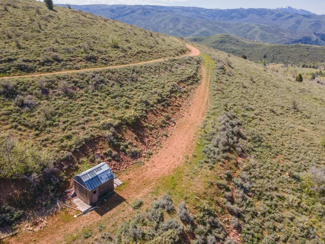 Unpaved roadway winding through a mountainous landscape with a small wooden structure featuring a metal roof
