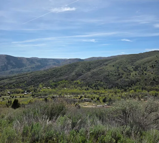 Expansive mountain landscape featuring rolling hills and abundant greenery under a vast blue sky