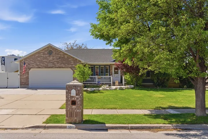 Brick exterior featuring an attached garage, covered front porch, and mature landscaping