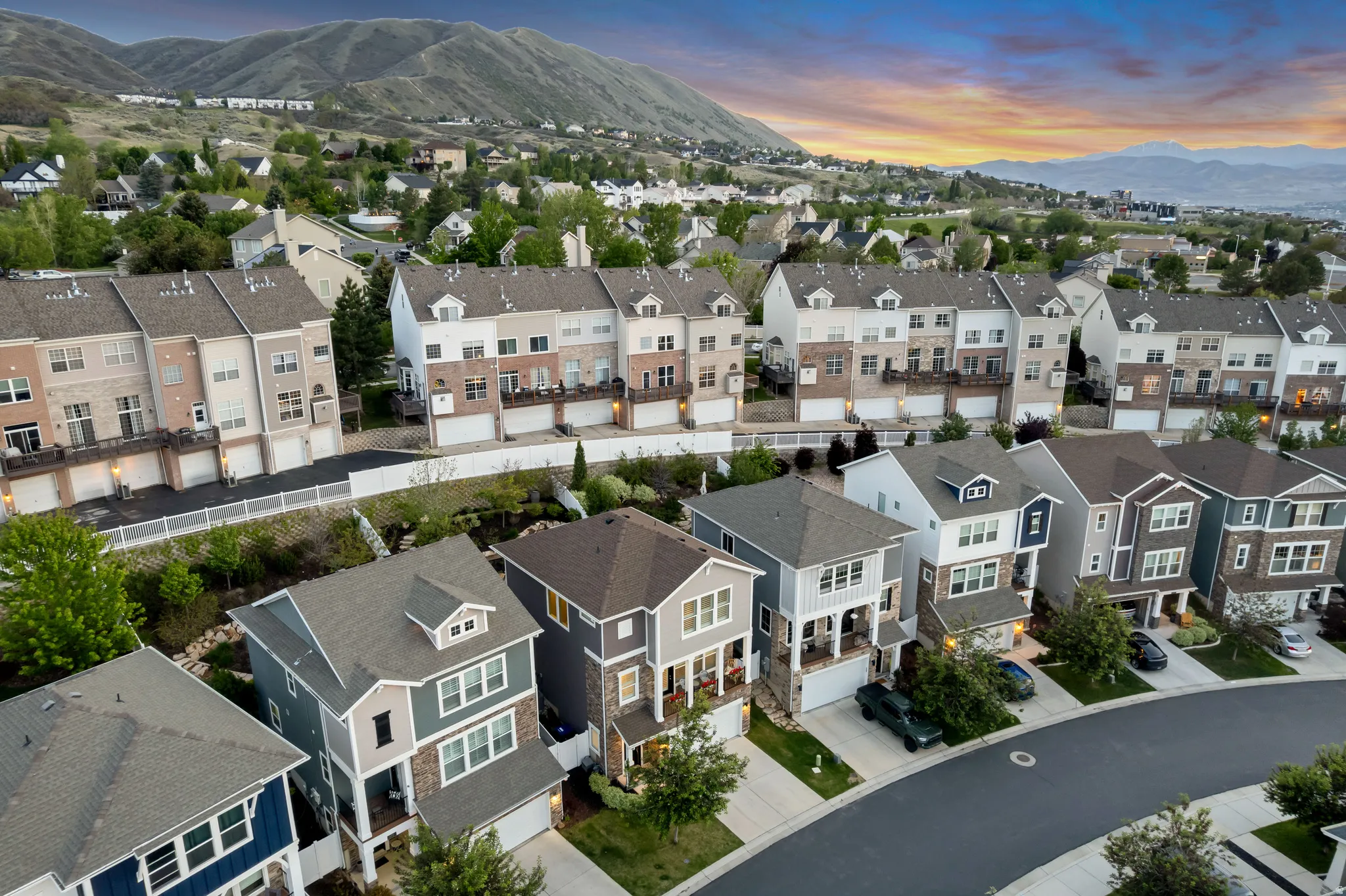 Residential streetscape featuring a curved road, varied home architectural styles, attached garages, and lush landscaping