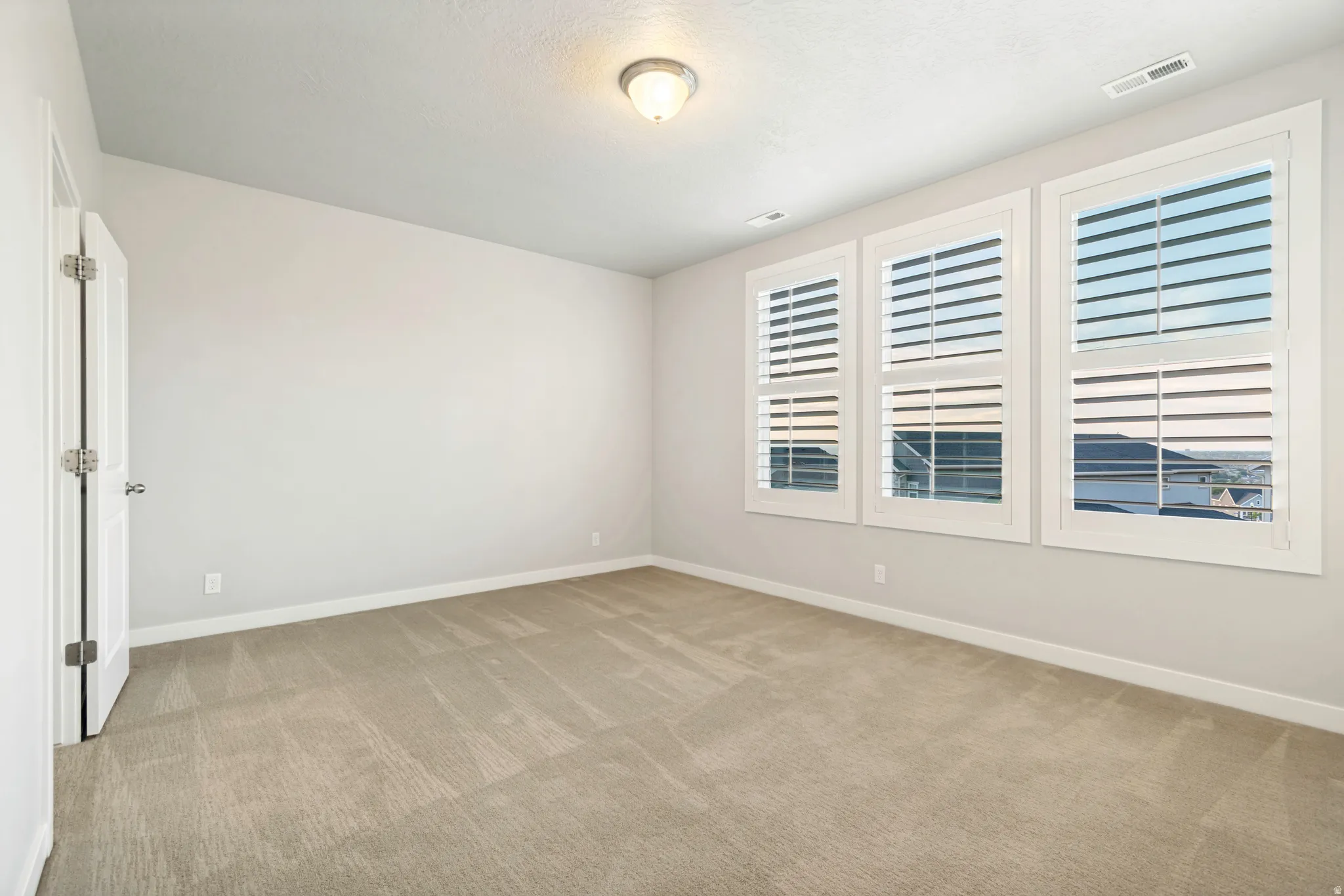 Carpeted room with three large windows featuring white plantation shutters