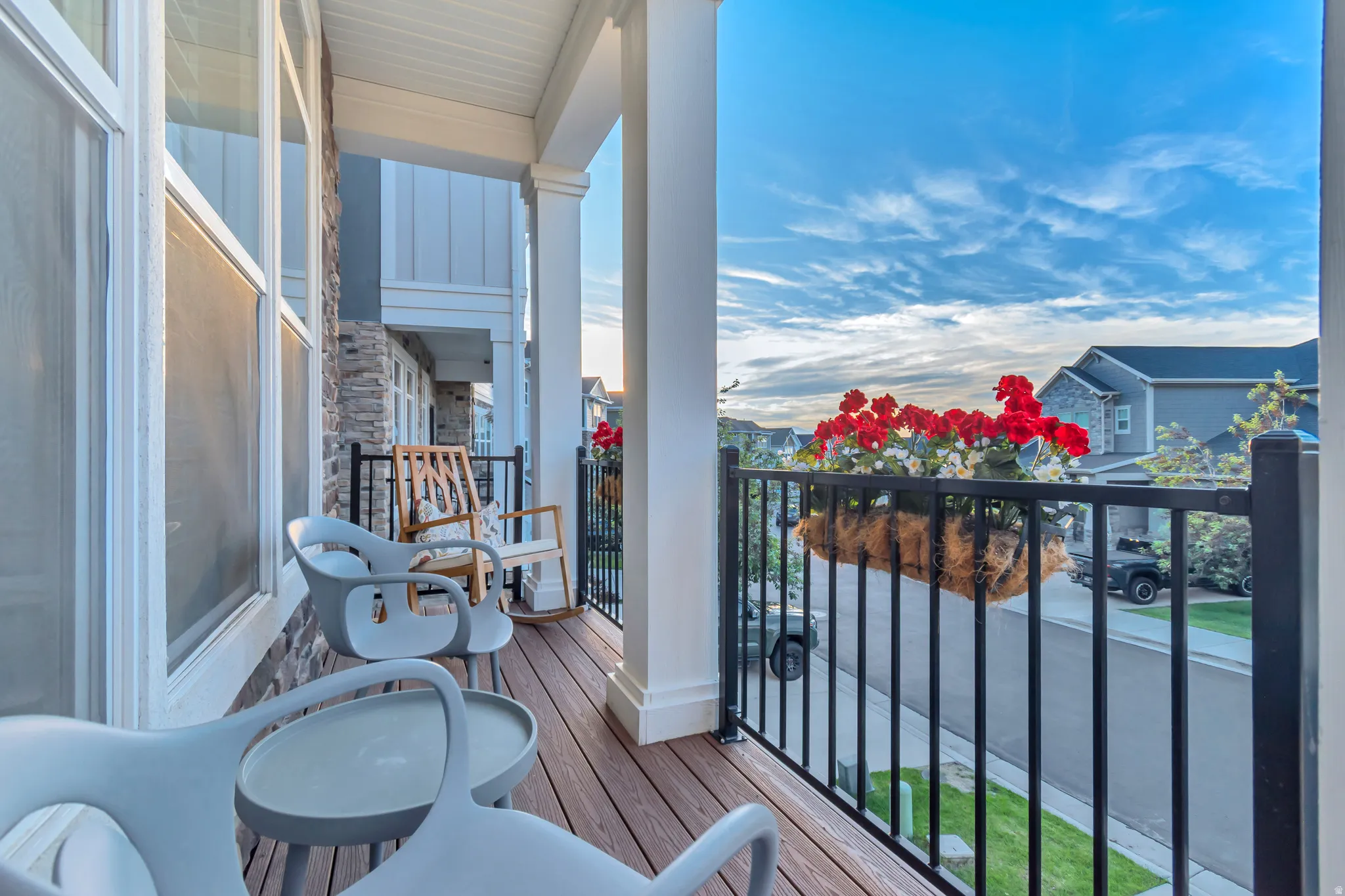 Covered front porch featuring wood-finish decking, white columns, and a black wrought iron railing