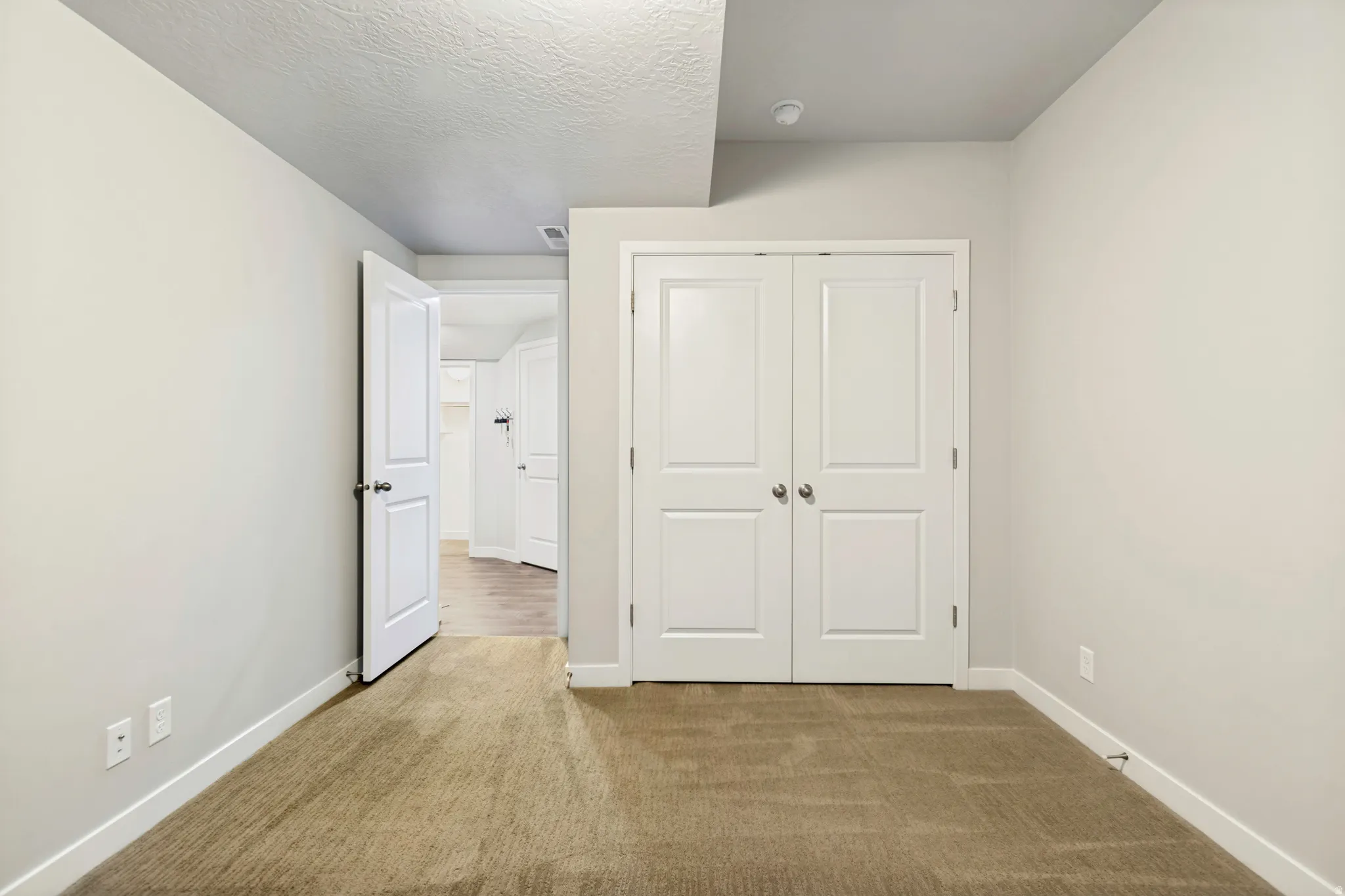 Neutral-toned room featuring a warm brown carpet, white baseboards, and a white six-panel bifold closet door