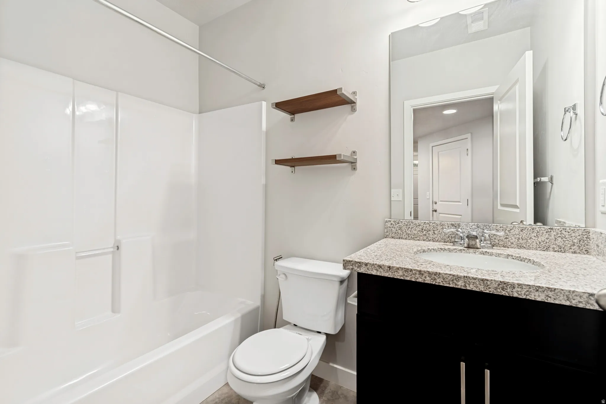 Bathroom featuring a white bathtub and shower surround, a toilet, and a vanity with a granite-style countertop