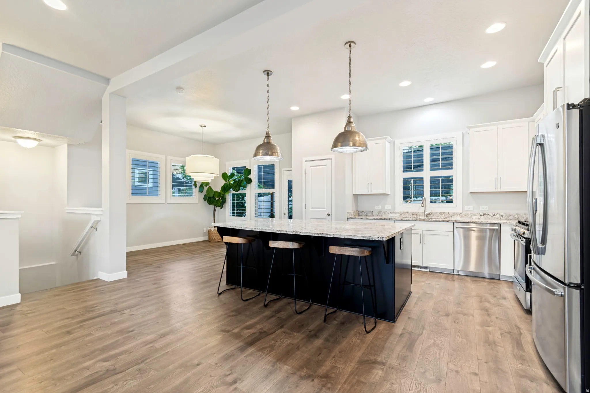 Open-concept kitchen featuring a dark-toned island with seating, pendant lighting, white cabinetry, stainless steel appliances, and light-toned wood-finish flooring