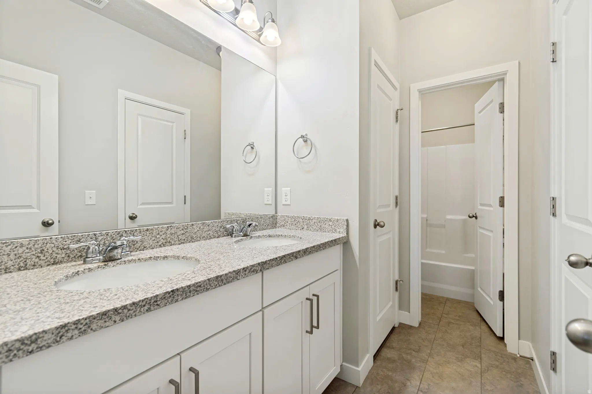 Bathroom featuring a dual vanity with granite-finish countertop, undermount sinks, chrome fixtures, and a large wall-mounted mirror