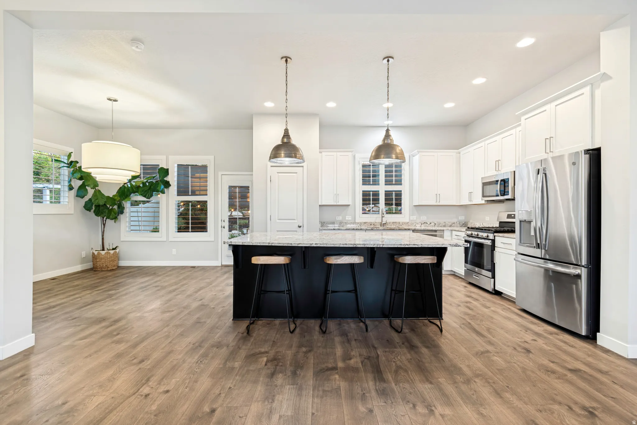 Open-concept kitchen featuring a dark-toned island with seating, pendant lighting, white cabinetry, and stainless-steel appliances
