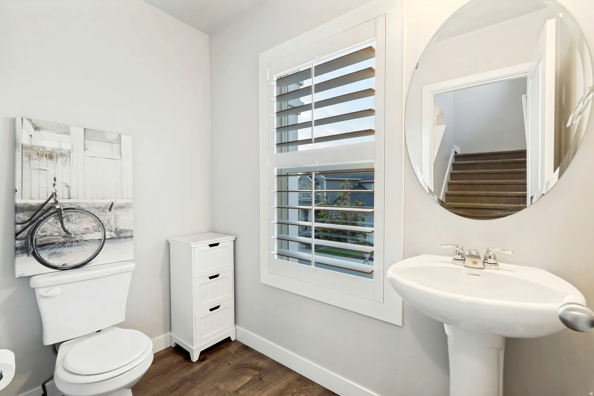 Pedestal sink with polished chrome fixtures, framed mirror, and wood-finish flooring