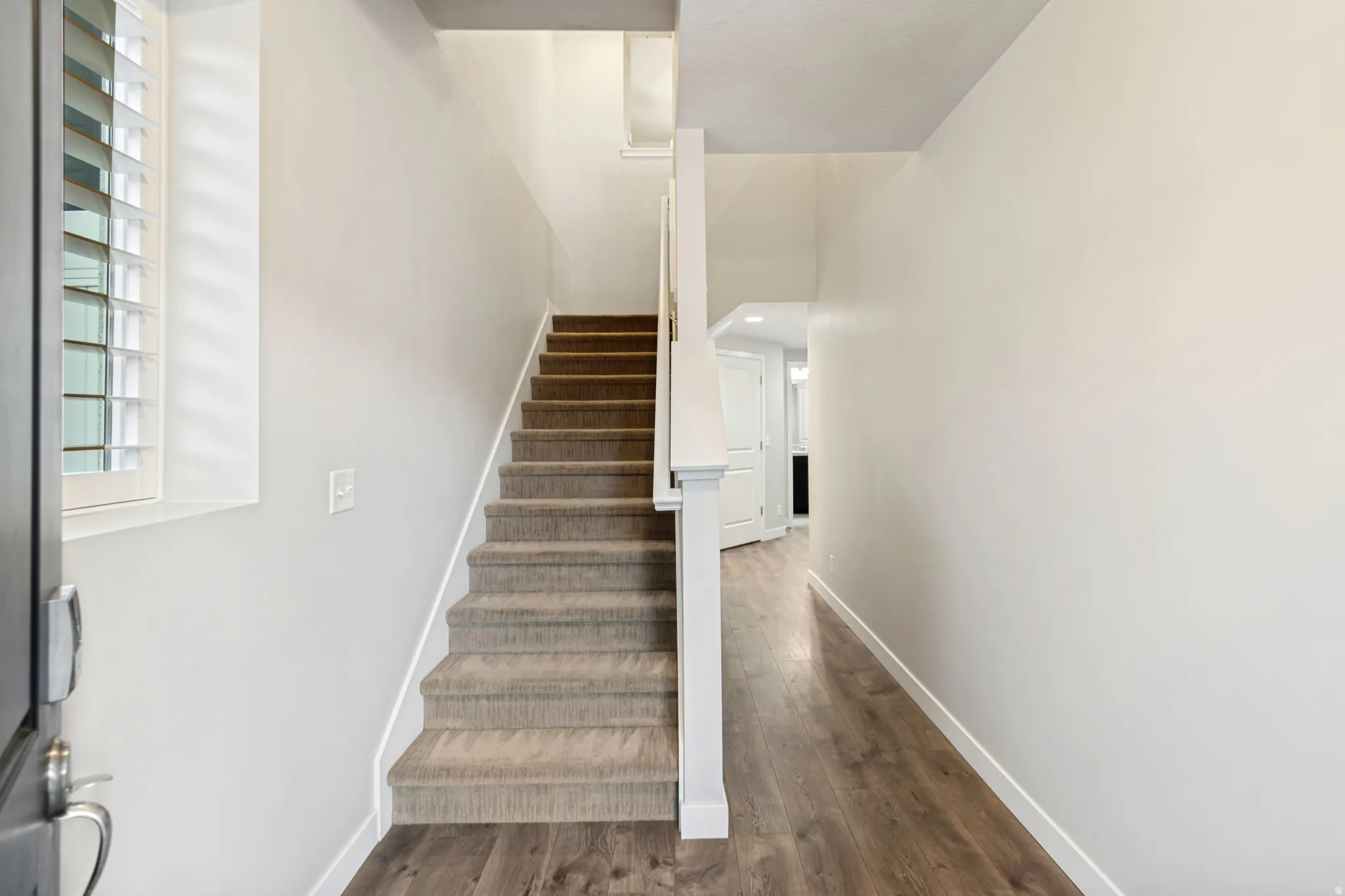 Entryway featuring wood-finish flooring, a carpeted staircase with white trim, and a window with plantation shutters