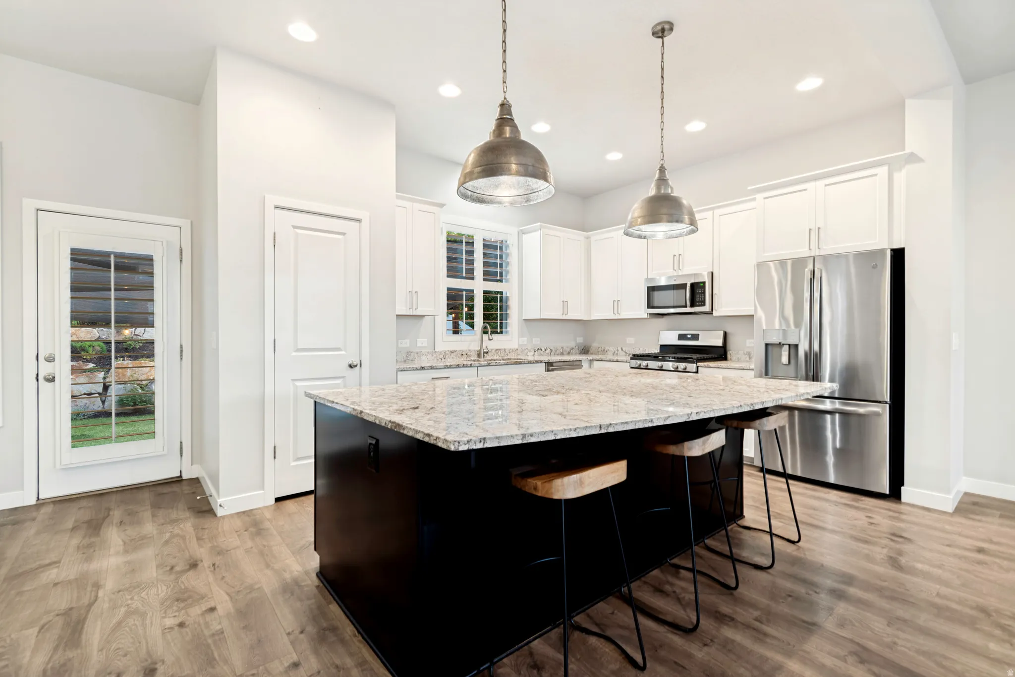 Open-concept kitchen featuring a spacious island with a light-colored countertop, white cabinetry, stainless steel appliances, and wood-finish flooring