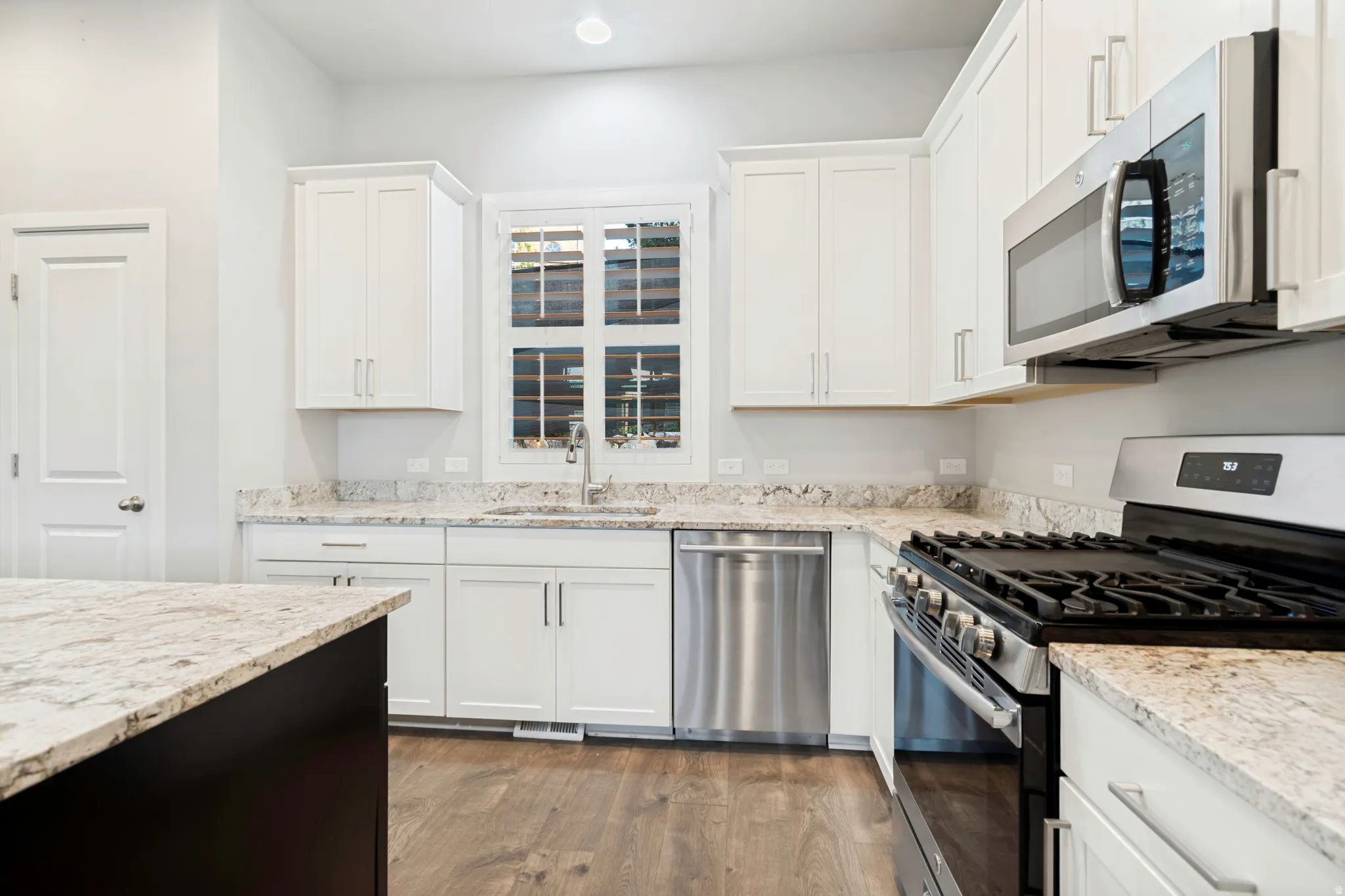 Kitchen featuring white cabinetry, light-toned granite countertops, stainless steel appliances, and wood-finish flooring