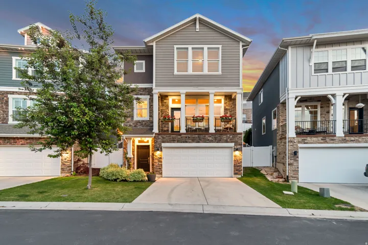 Contemporary townhome featuring a stone and siding exterior, integrated two-car garage, covered entry, and an upper-level balcony with wrought iron railing