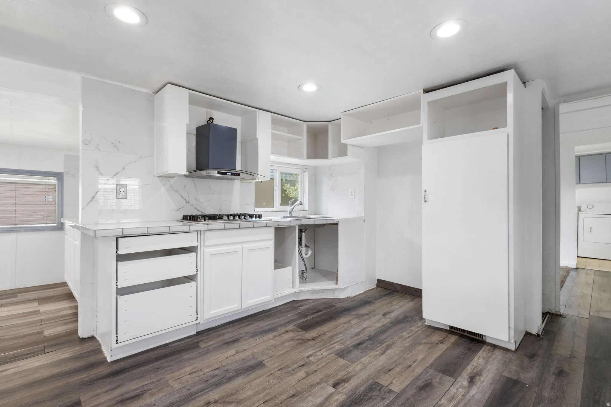 Contemporary kitchen featuring LVP flooring, white cabinetry, a gas cooktop with a range hood, and a white tile backsplash