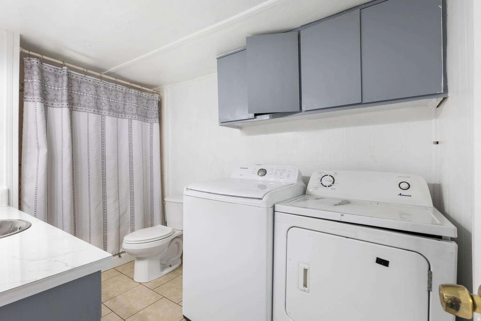 Laundry area featuring white appliances, upper storage cabinetry, and tiled flooring