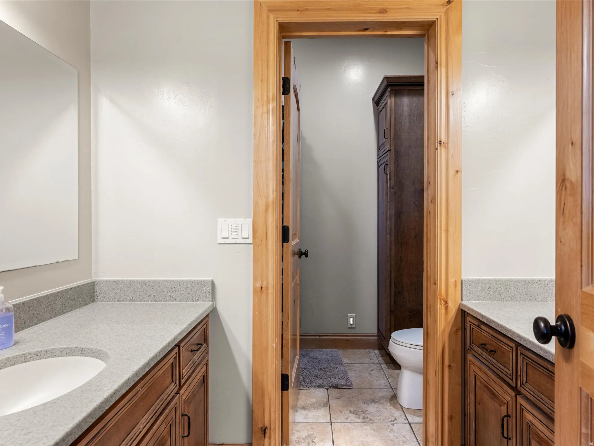 Bathroom vanity featuring a light-toned countertop with integrated sink, dark wood-finish cabinetry, and a full-width mirror