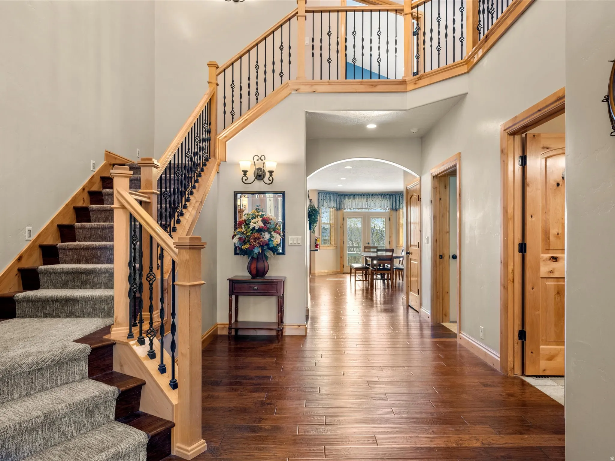 Two-story entryway featuring a grand staircase with wrought iron balusters and natural wood newel posts