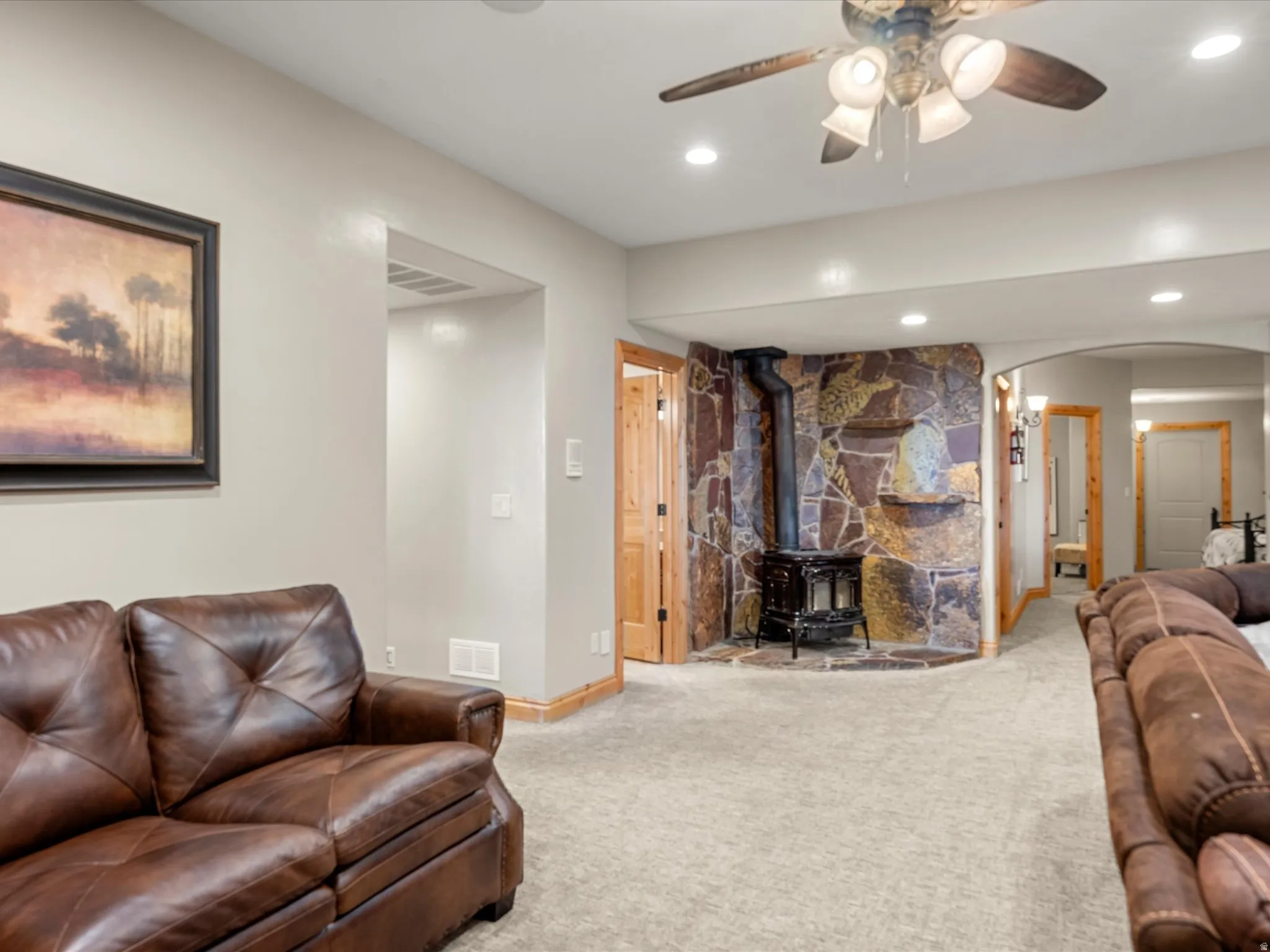 Spacious room featuring a stone-clad wall with a wood-burning stove, recessed lighting, and a ceiling fan