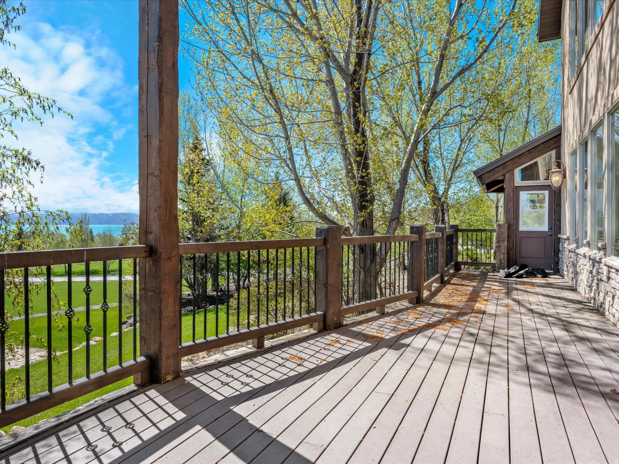 Spacious outdoor deck featuring wood-finish flooring, robust wooden railings with decorative metal balusters, and a natural stone-clad exterior wall