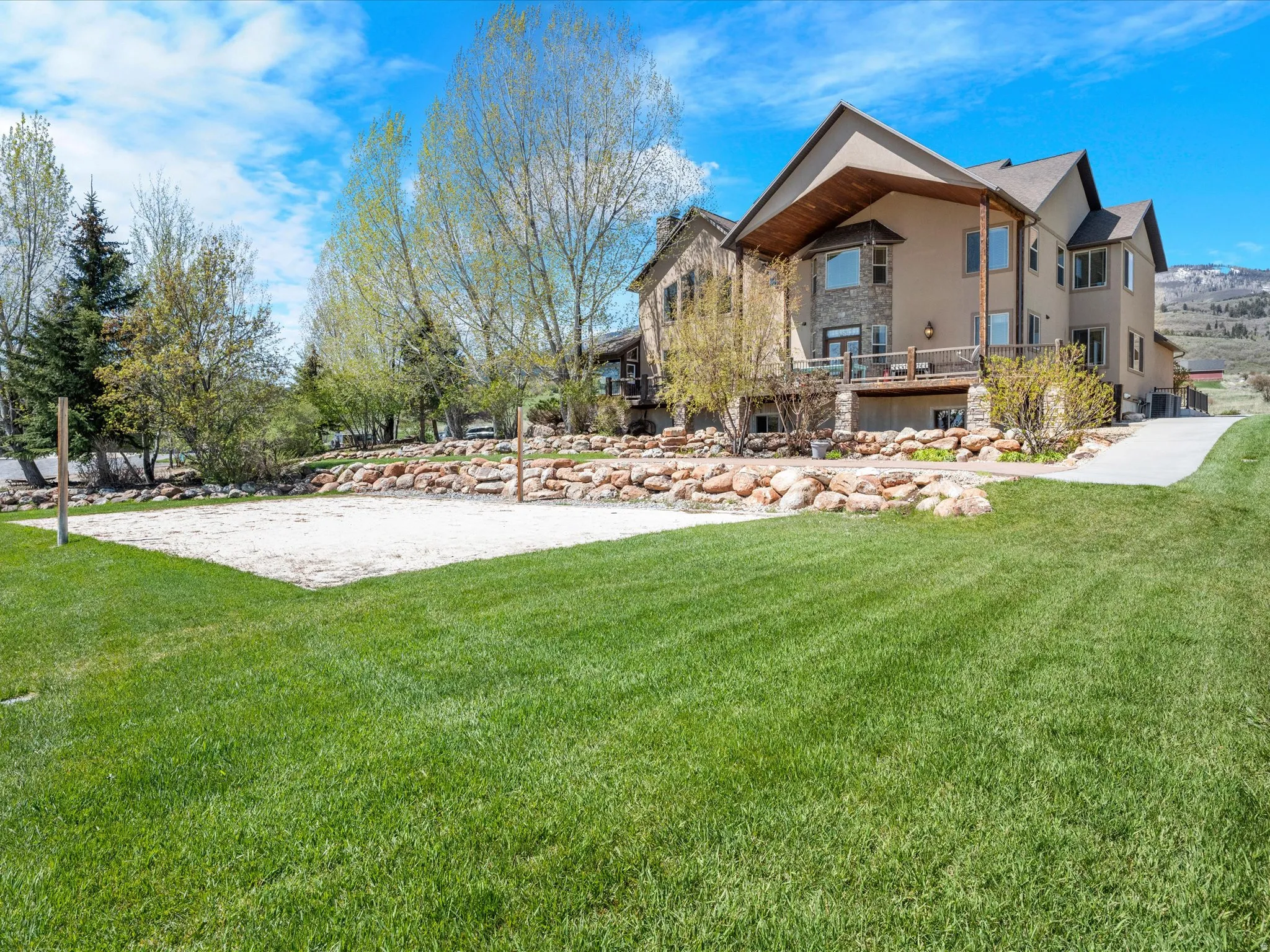 Expansive rear grounds with a sand court, natural rock landscaping, and a sloped lawn