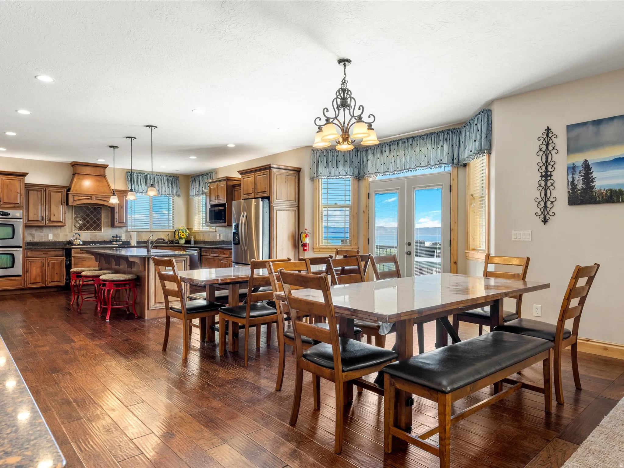 Open-concept dining area featuring wood-finish flooring, a decorative chandelier, and double French doors opening to an outdoor area