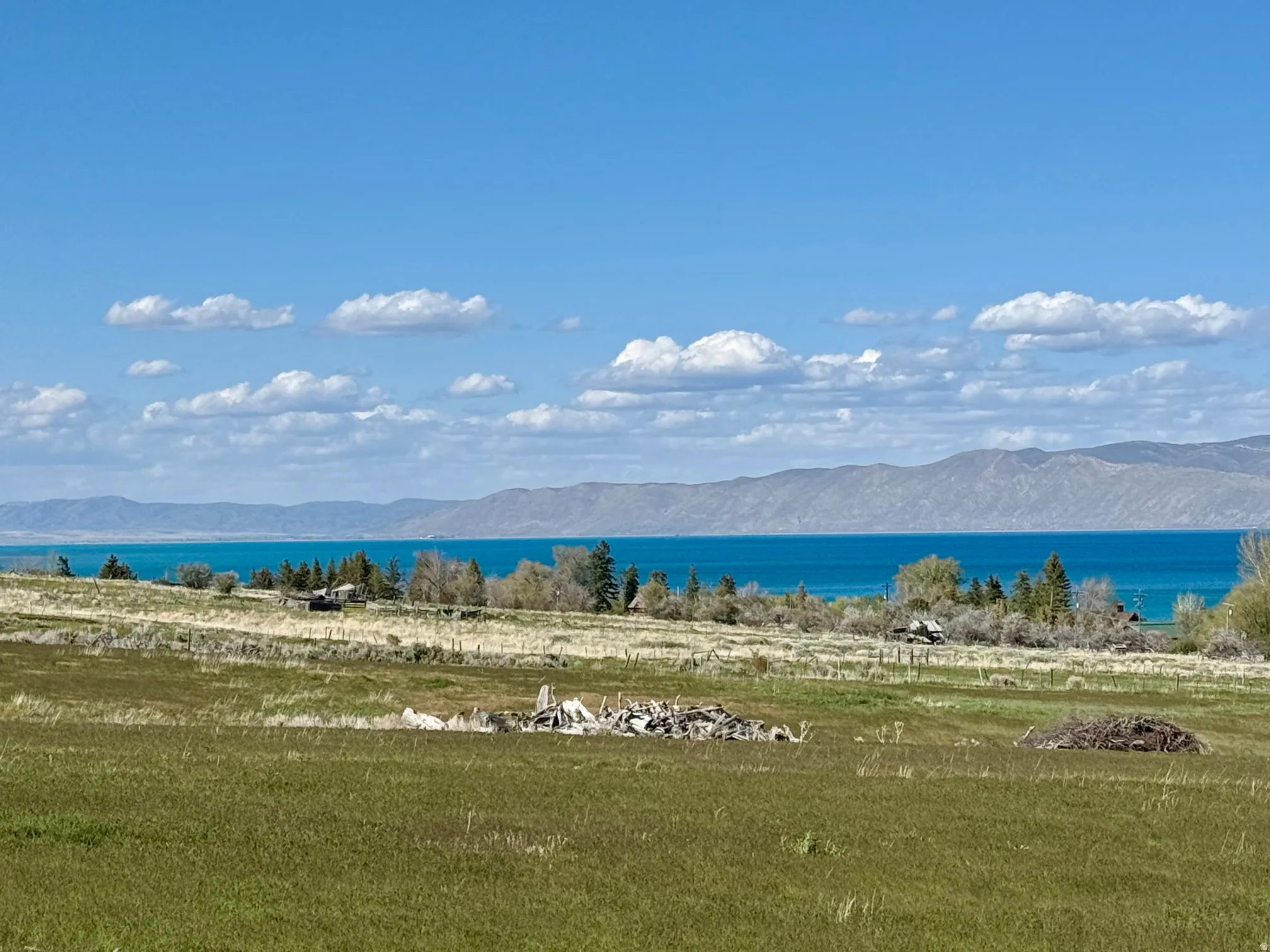 Expansive undeveloped land featuring a broad field, natural foliage, distant mountain ranges, and a large body of water