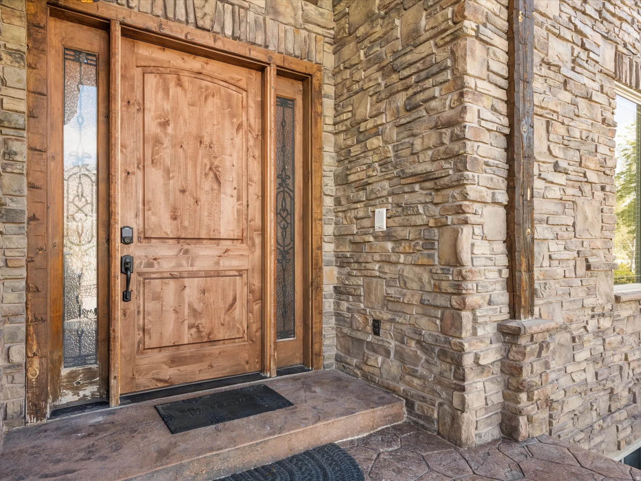 Solid wood entry door with decorative glass sidelights, set within a stone-clad exterior