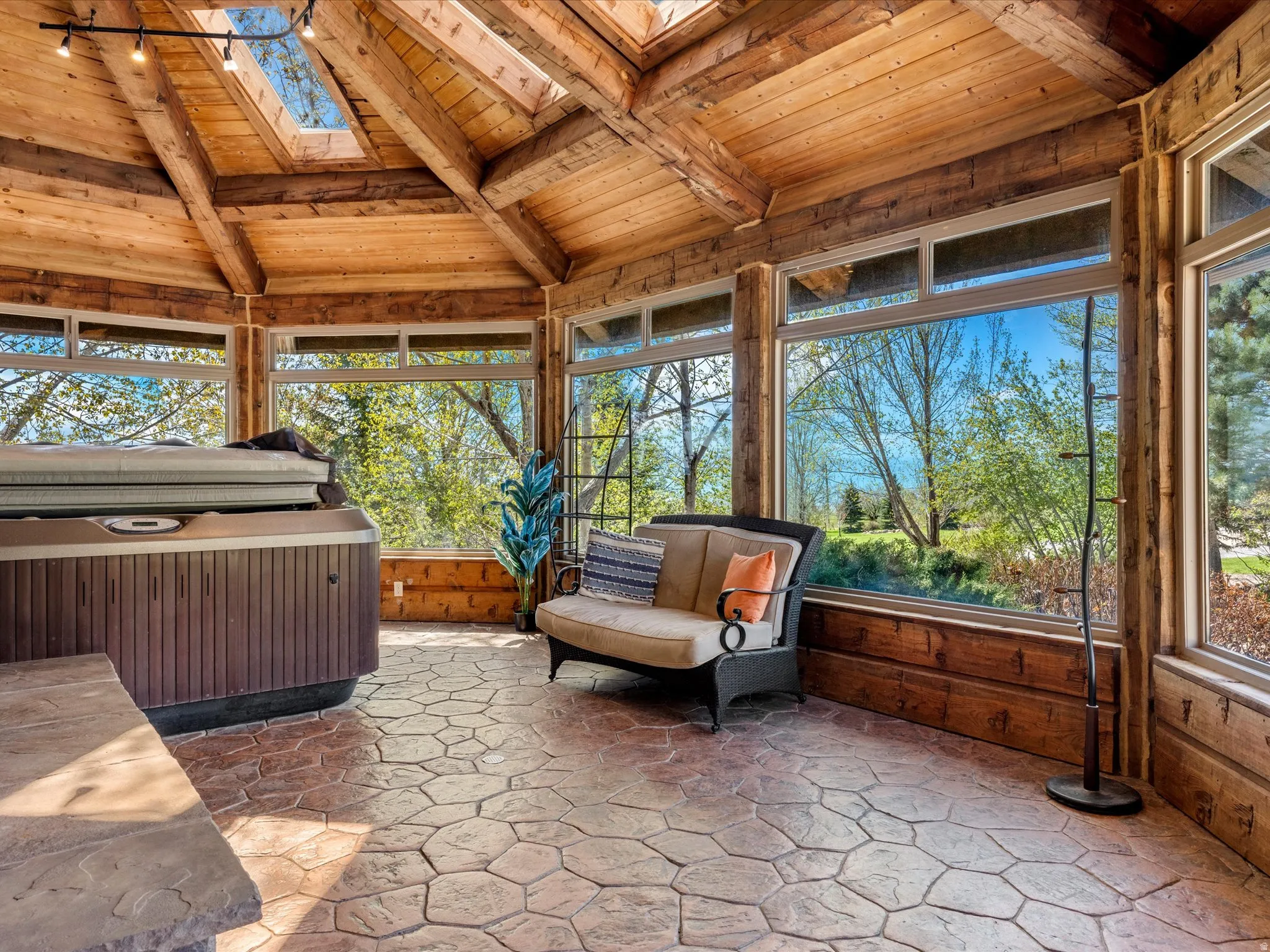 Expansive sunroom featuring a hot tub, stone-patterned flooring, exposed wood beam ceiling, and skylights