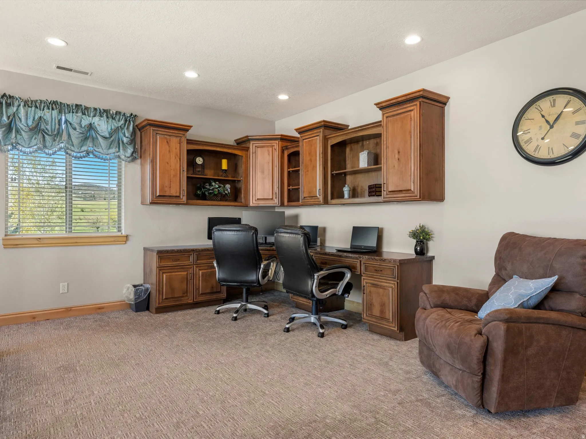 Dedicated workspace featuring extensive built-in cabinetry, dual workstations, recessed lighting, and a large window