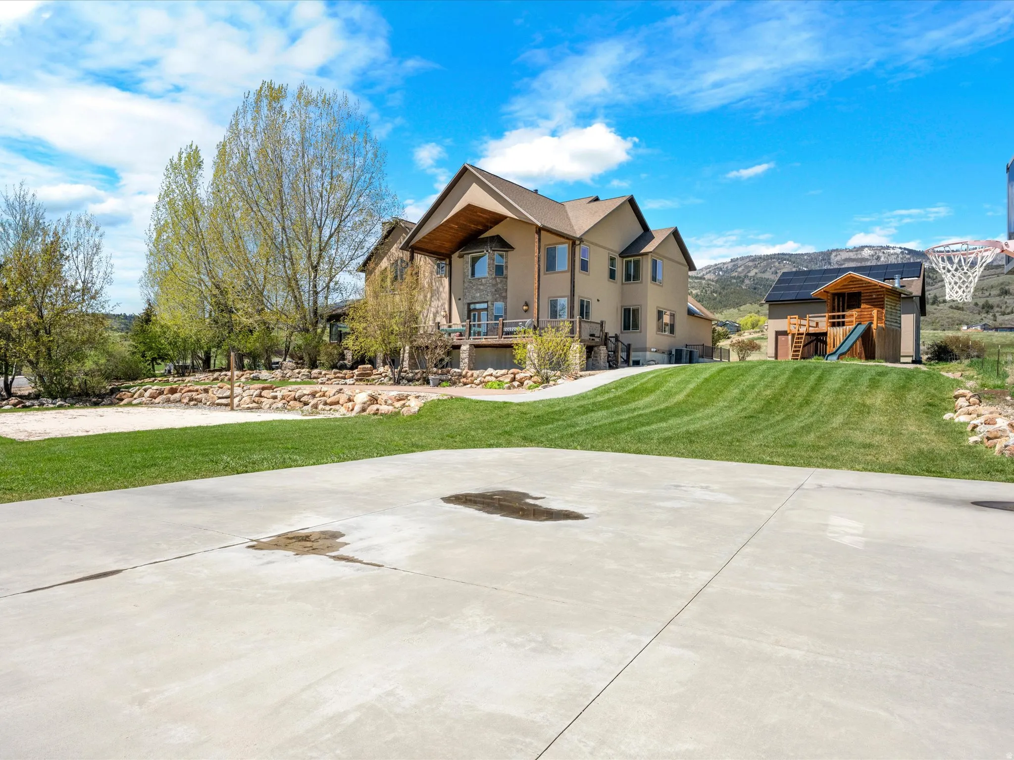 Expansive concrete driveway leading to a multi-story residence with stone accents and a covered balcony