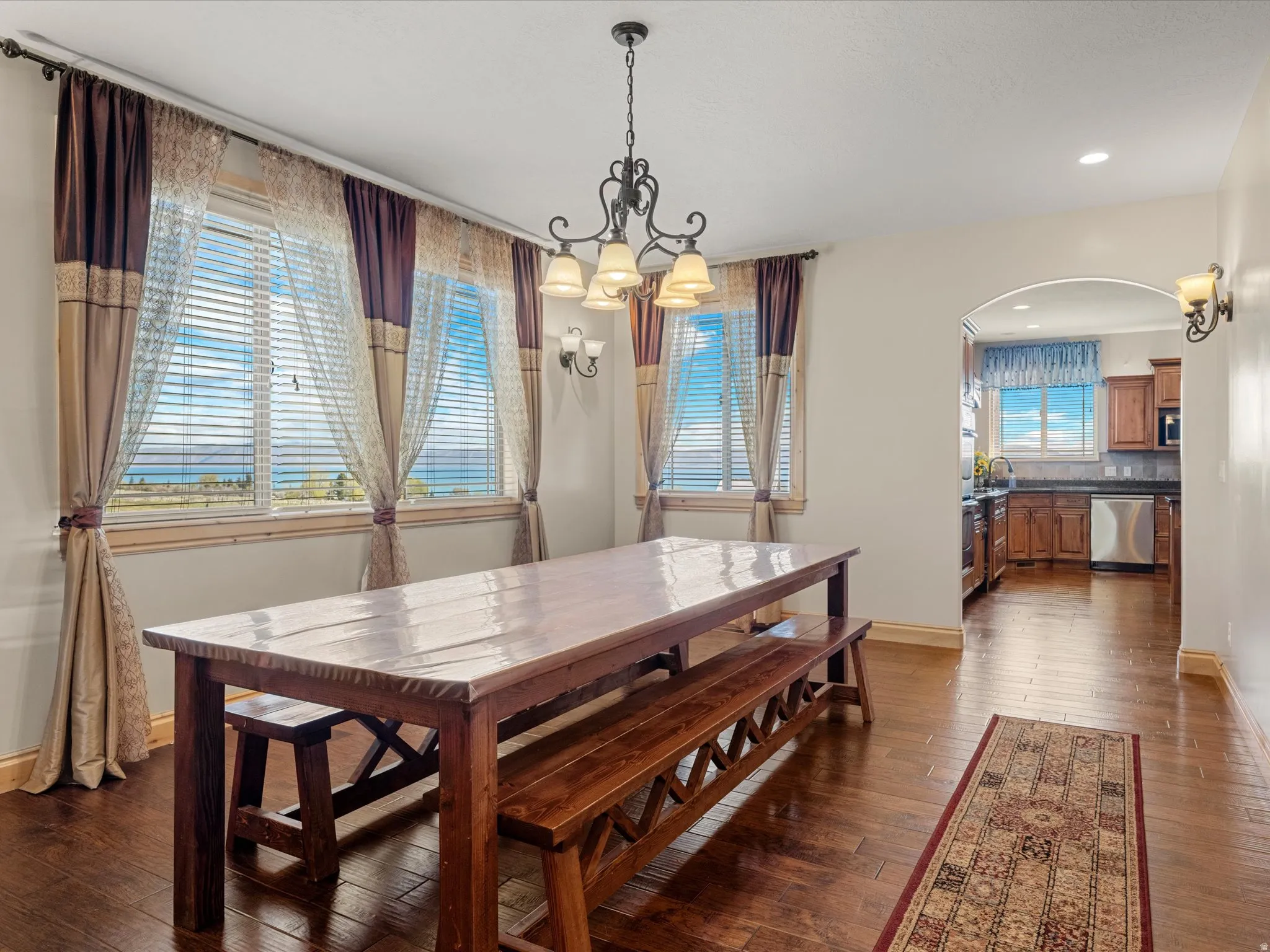 Formal Dining area featuring rich wood-finish flooring, an ornate iron chandelier, and dual windows with horizontal blinds