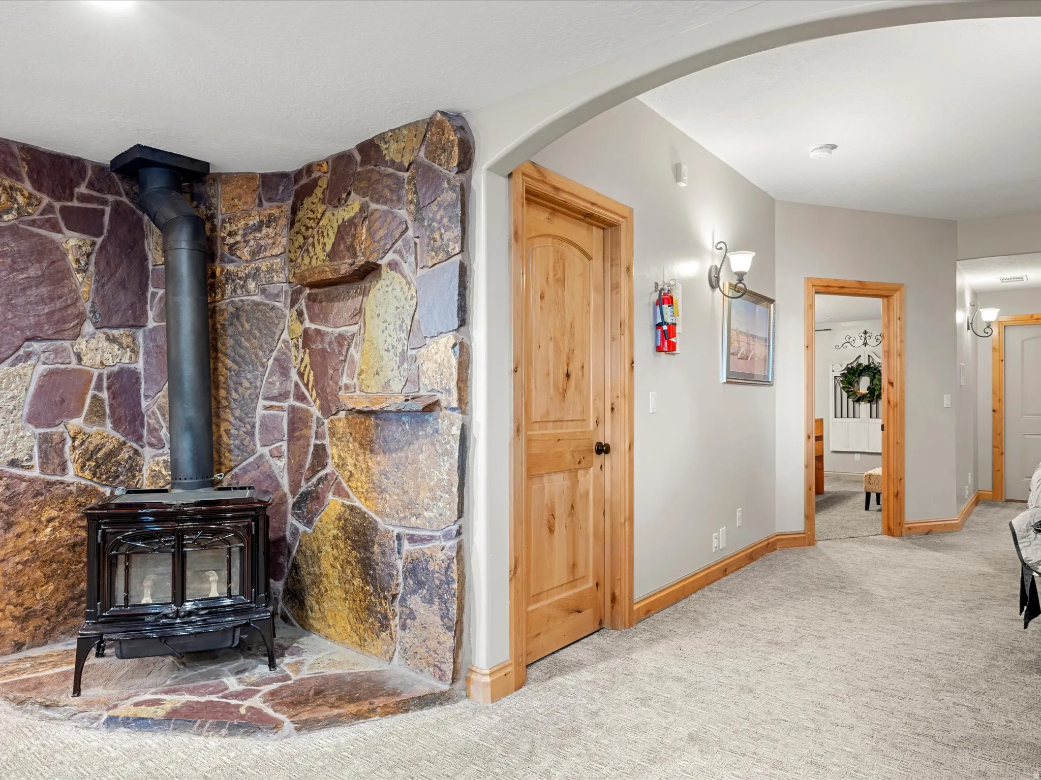 Stone accent wall featuring a black wood-burning stove with a metal flue