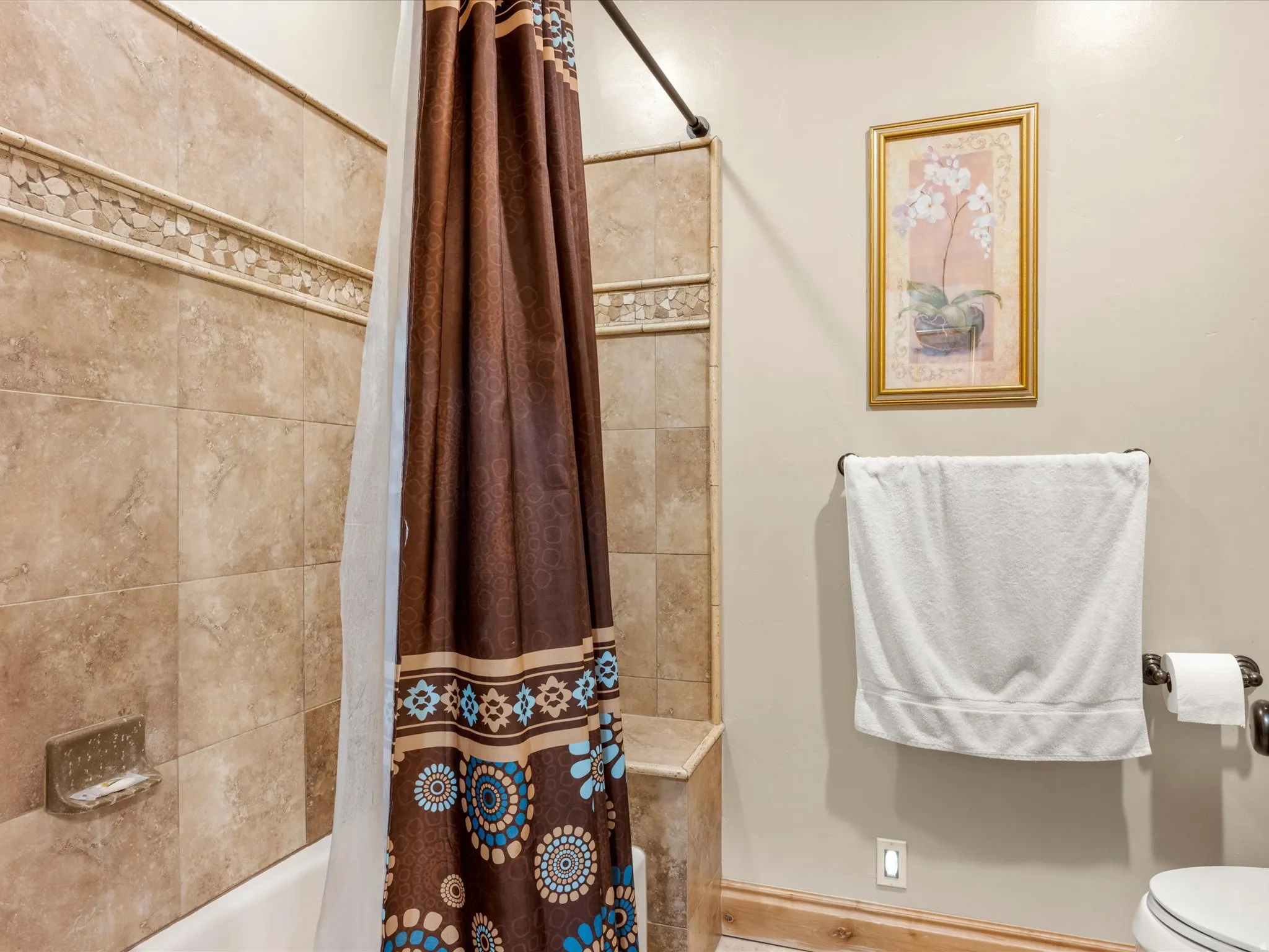 Bathtub and shower combination featuring neutral-toned tile surround with decorative accent band and built-in bench