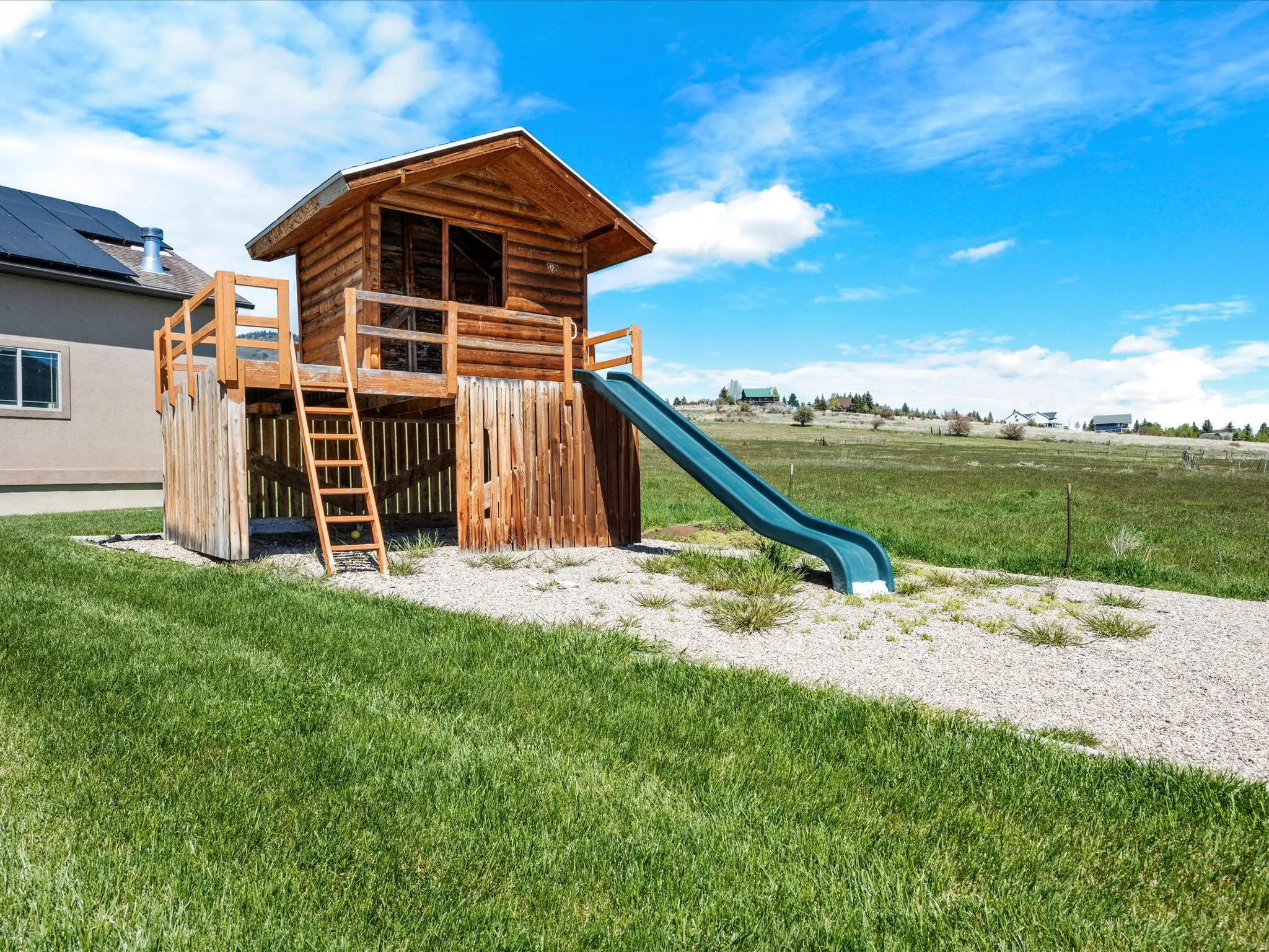 Detached wooden play structure featuring a log cabin design, raised platform, ladder access, and an attached slide